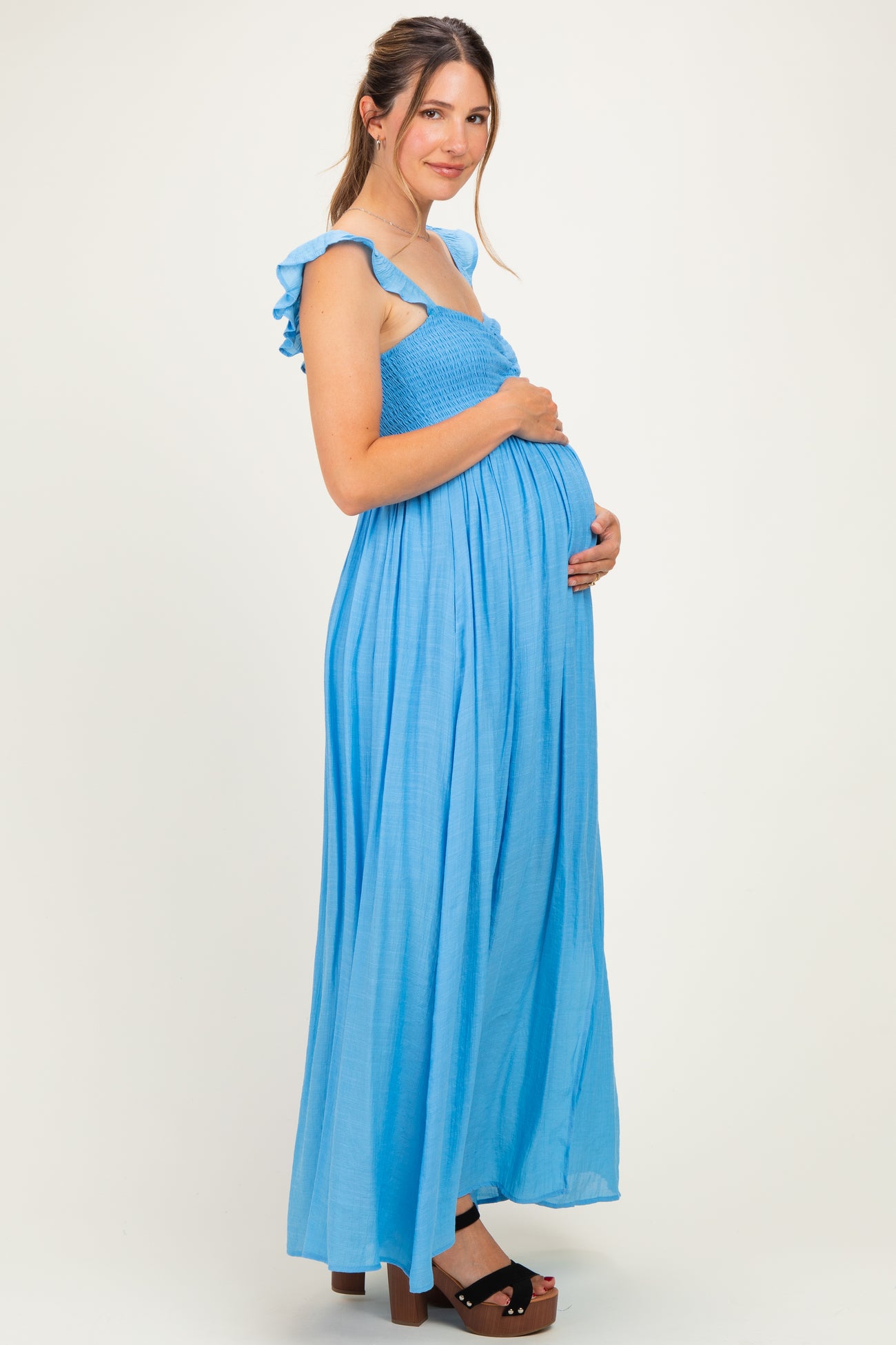 woman wearing a sky blue maternity maxi dress with ruffled straps and holding her baby bump