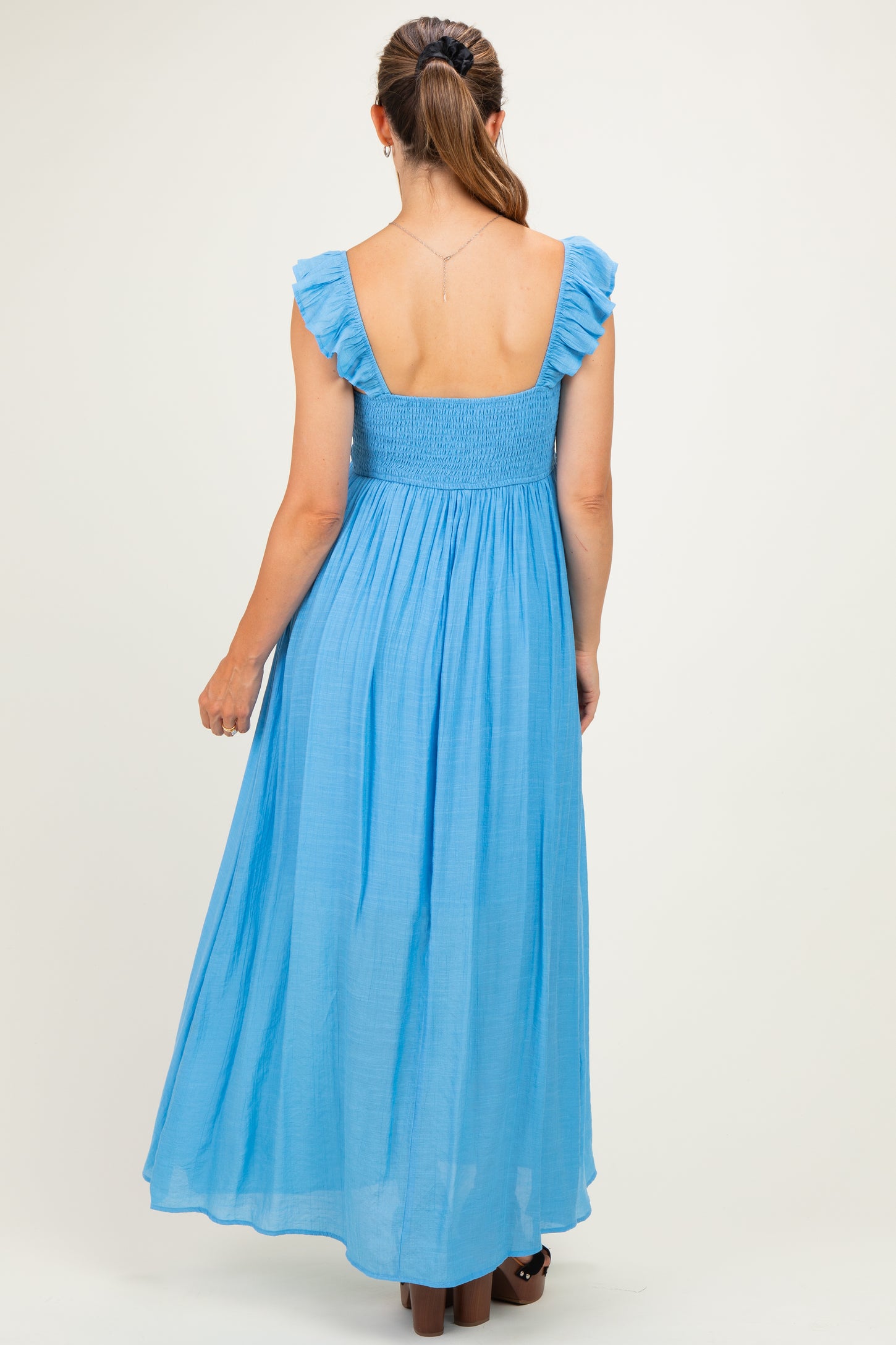 woman wearing a light blue maternity maxi dress with ruffle sleeves and a smocked bodice, showing her back