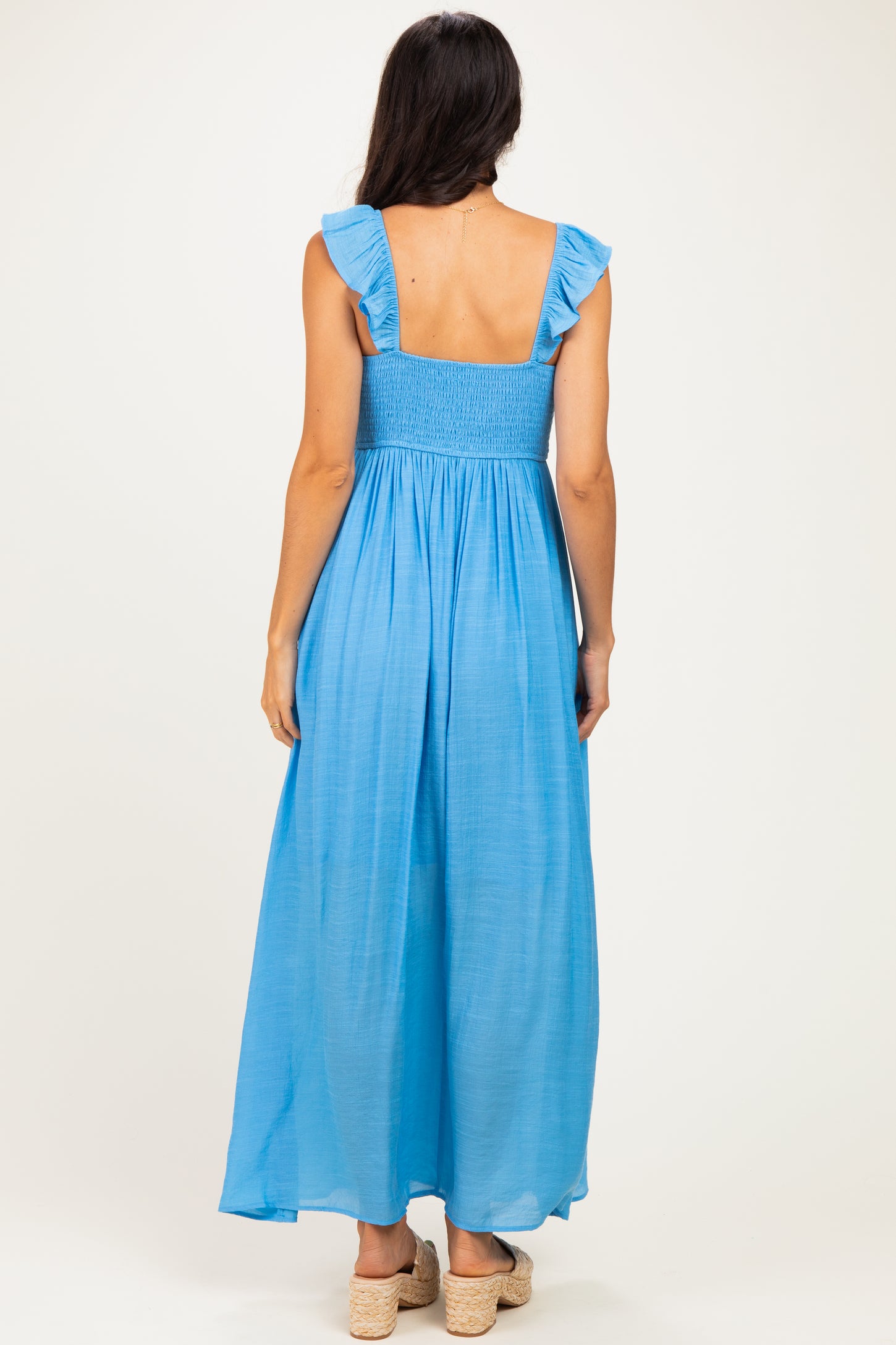 woman wearing a sleeveless blue maxi dress with ruffle straps and a smocked bodice, seen from the back