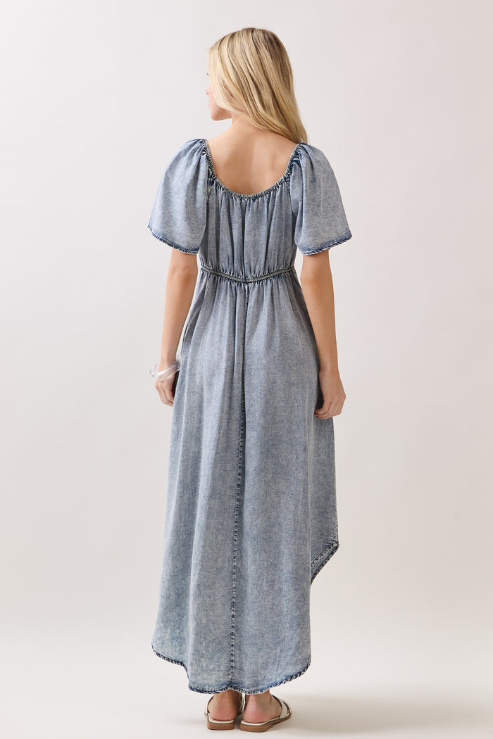 woman wearing a light blue puff sleeve maxi dress with a cinched waist and a flowy skirt, standing with her back to the camera