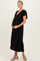 woman wearing a black maternity maxi dress with flutter sleeves and a v-neck, showcasing her baby bump
