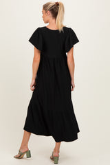 woman wearing a black maternity maxi dress with a tiered skirt and flutter sleeves, showing her back
