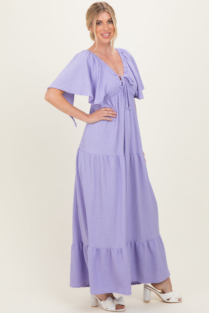 woman wearing a lavender maxi dress with flutter sleeves and a tie front detail, posing against a neutral background