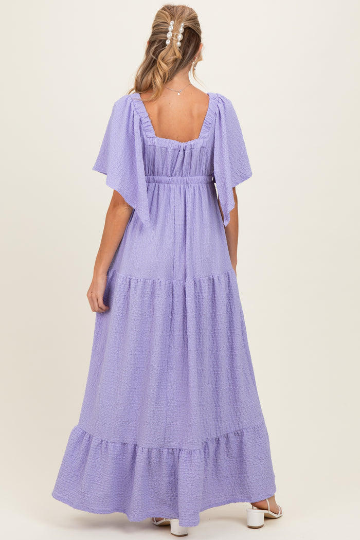 woman wearing a lavender maternity maxi dress with flutter sleeves and tiered ruffle details, viewed from the back