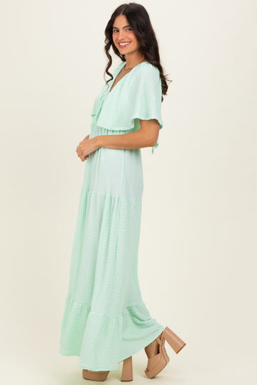 woman wearing a light green maxi dress with ruffle sleeves and tiered skirt, standing in profile