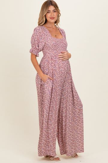 woman wearing a pink floral maternity maxi dress with short puff sleeves and pockets, gently cradling her baby bump