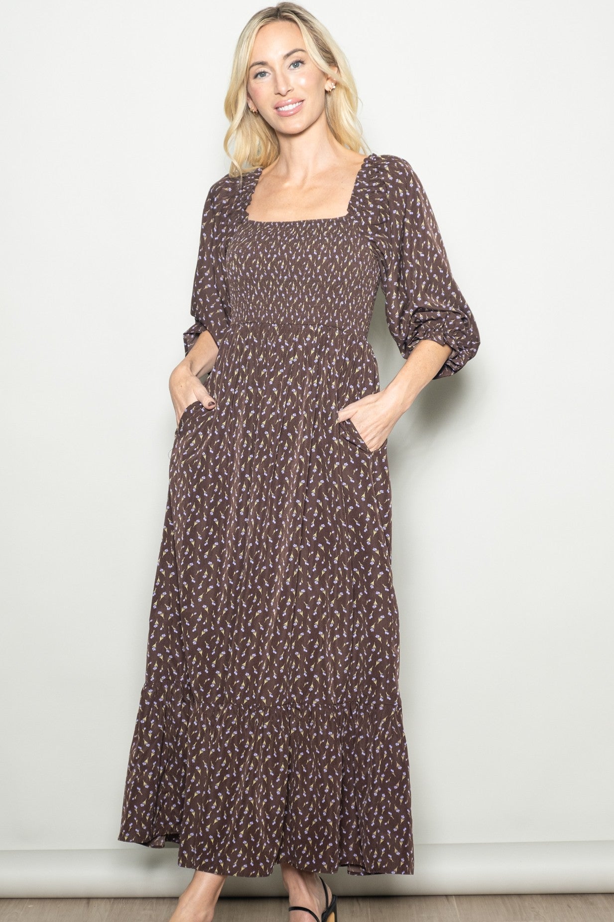 woman wearing a brown floral maxi dress with puff sleeves and a smocked bodice, featuring pockets and a tiered skirt