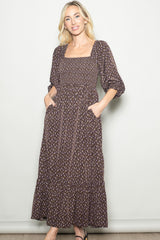 woman wearing a brown floral maxi dress with puff sleeves and a smocked bodice, featuring pockets and a tiered skirt
