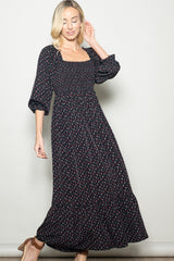 woman wearing a black floral maxi dress with a square neckline and puff sleeves, standing elegantly
