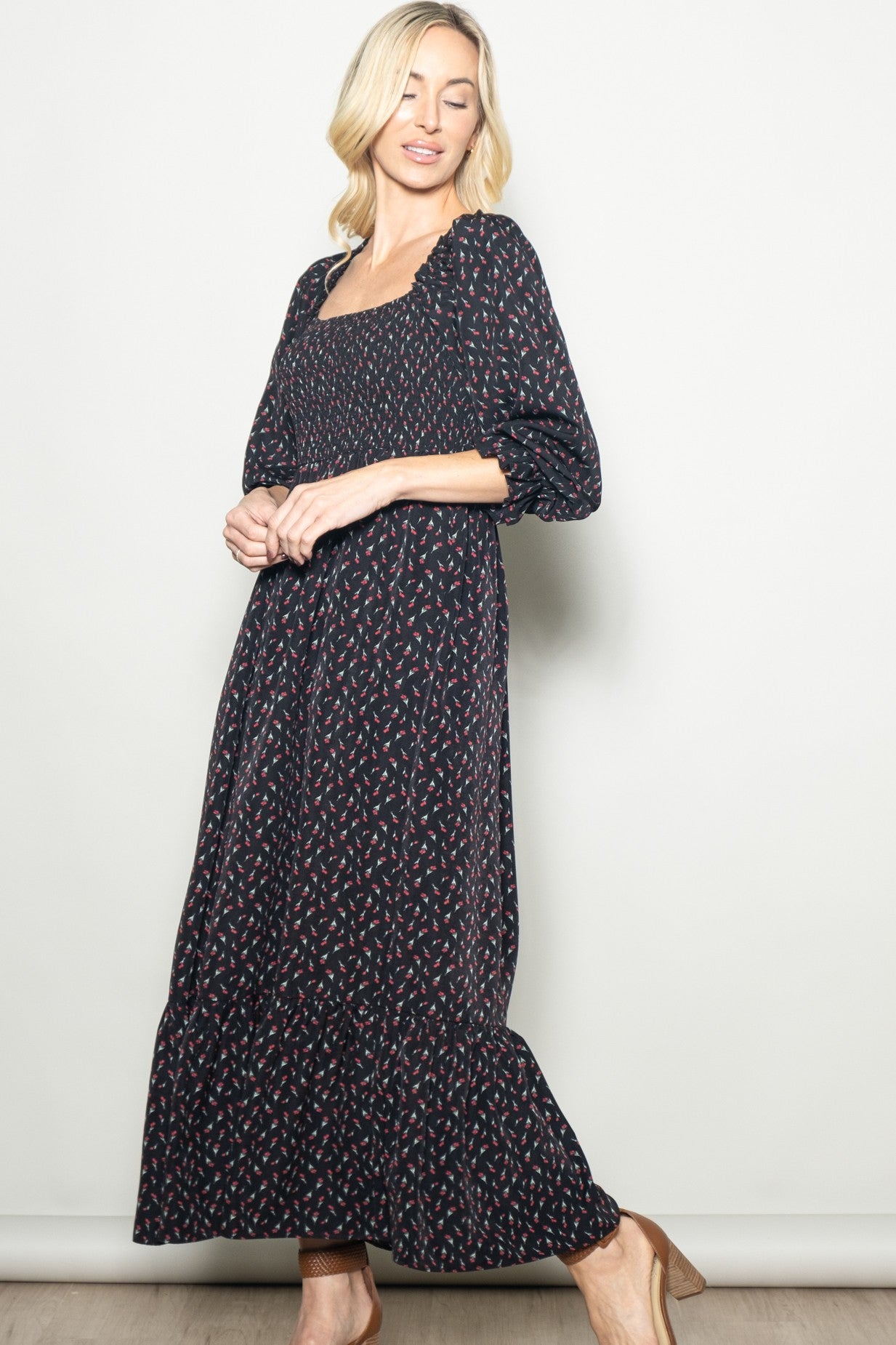 woman wearing a black maxidress with floral print and puff sleeves, standing against a neutral background