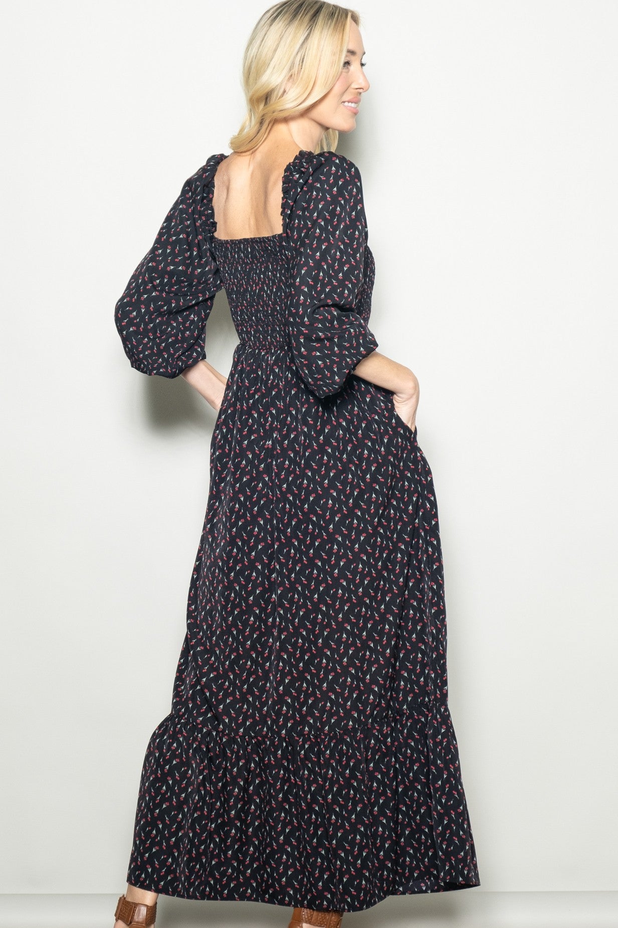 woman wearing a black floral maxi dress with puff sleeves and a smocked bodice, standing with hands in pockets