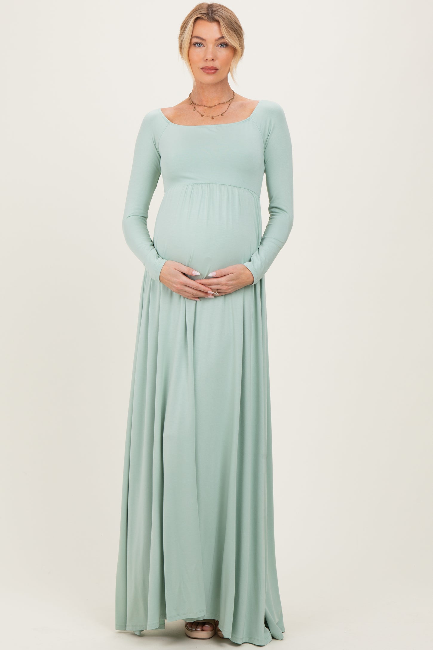woman wearing a light green long sleeve maternity maxi dress and holding her baby bump