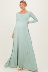 woman wearing a mint green long sleeve maternity maxi dress with a fitted bodice and flowy skirt, showing her baby bump