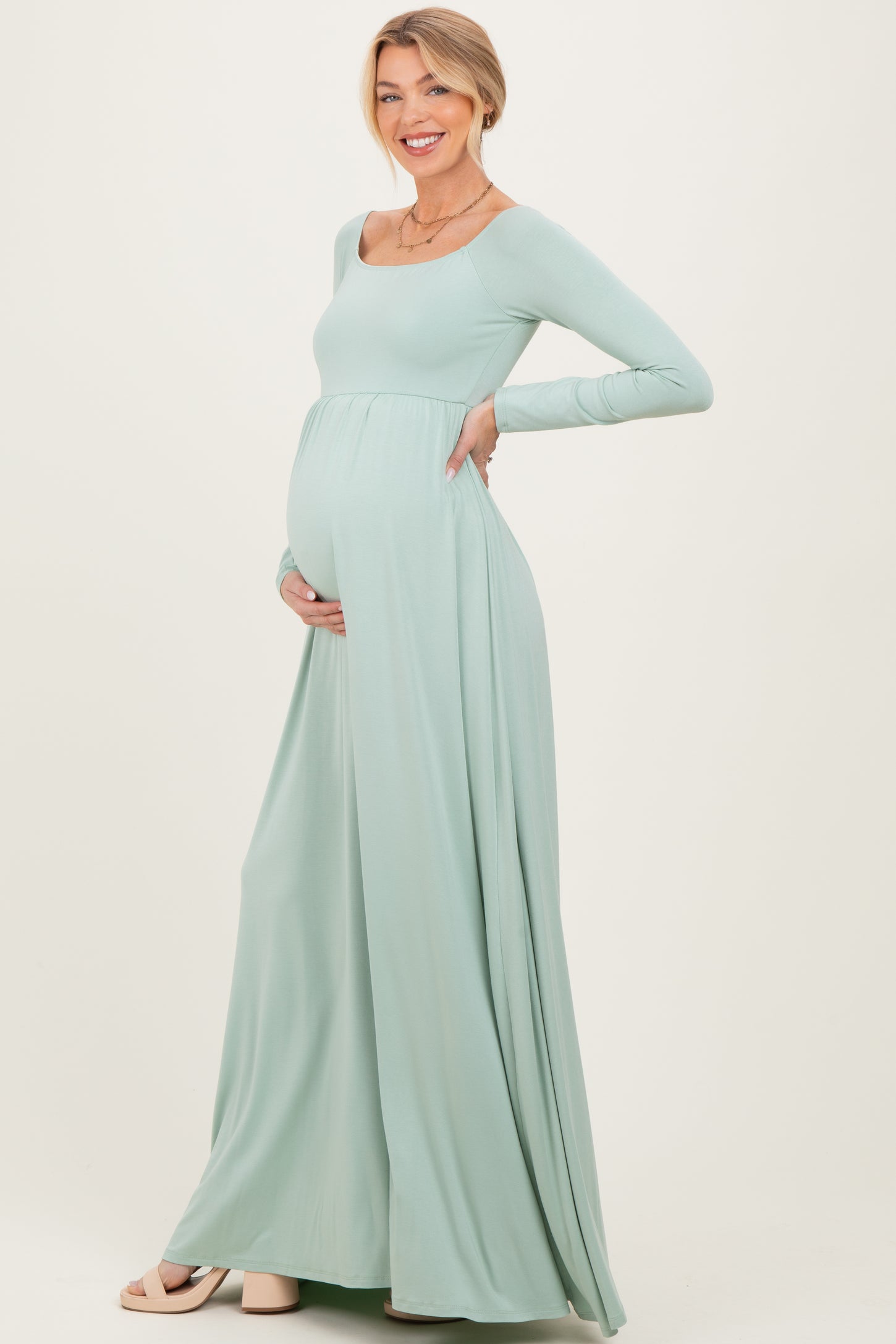 woman wearing a mint green long sleeve maternity dress and cradling her baby bump