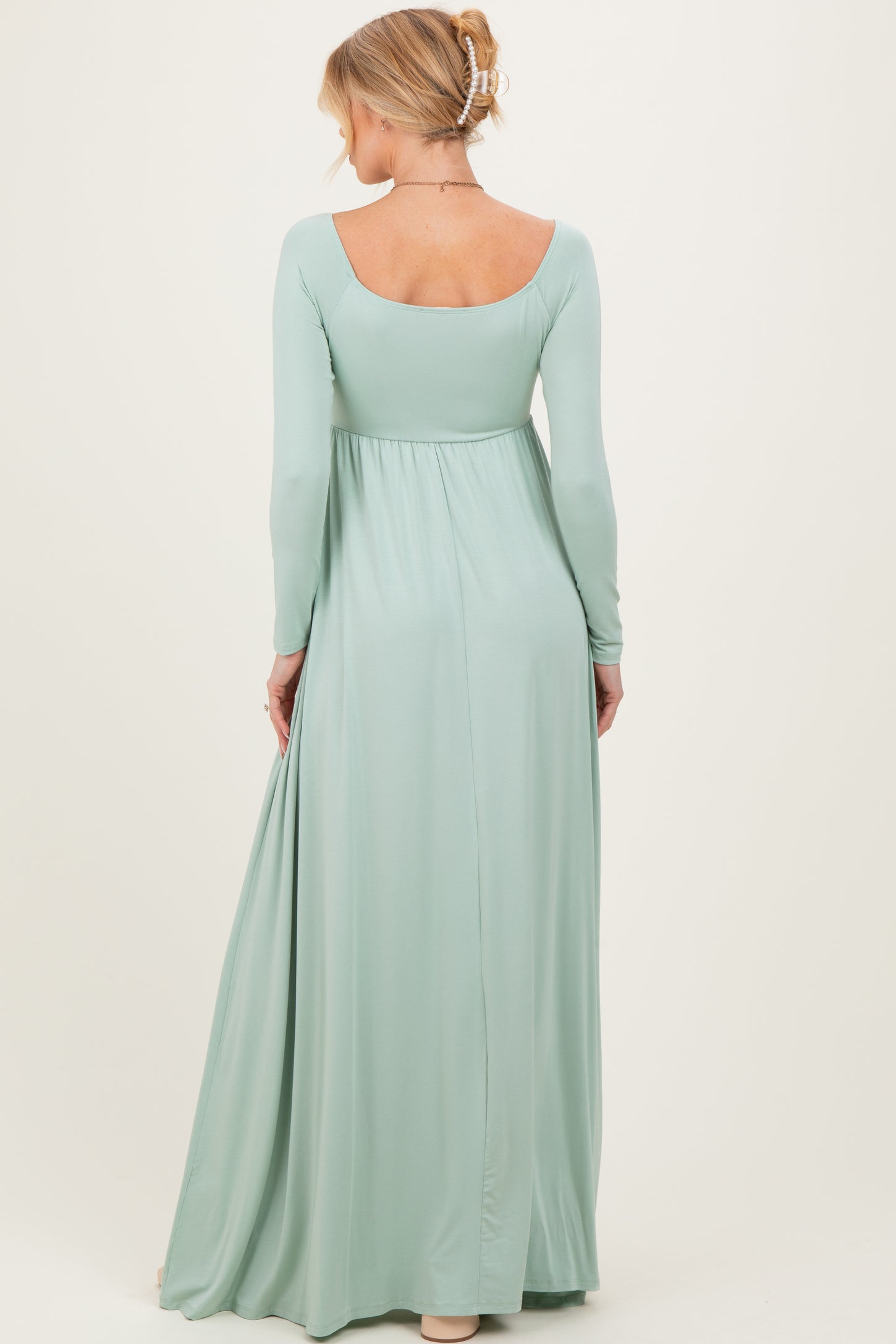 woman wearing a long sleeve mint green maternity maxi dress, showing her back and flowing fabric