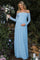 woman wearing a light blue off-shoulder lace maternity gown and holding her baby bump with a bouquet of flowers