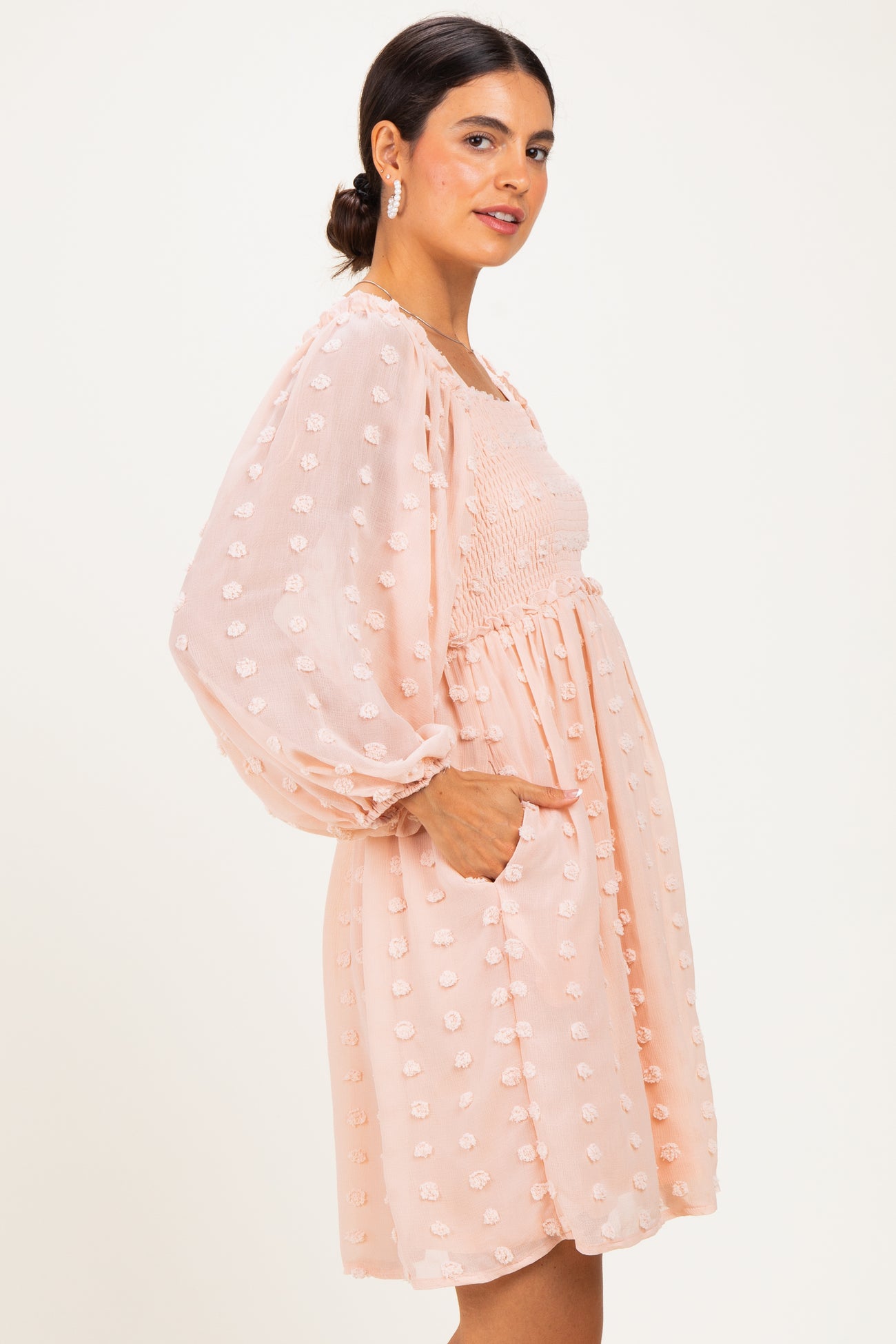 woman wearing a light peach puff sleeve mini dress with textured floral details and pockets