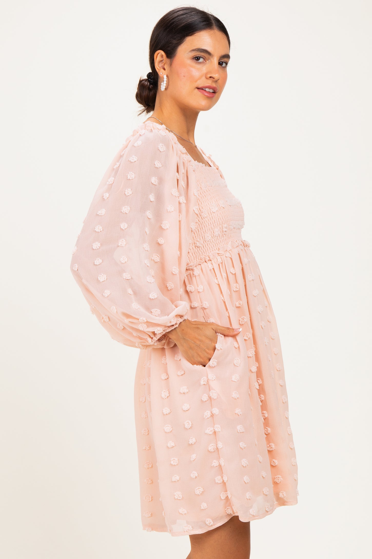 woman wearing a light peach puff sleeve mini dress with textured floral details and pockets