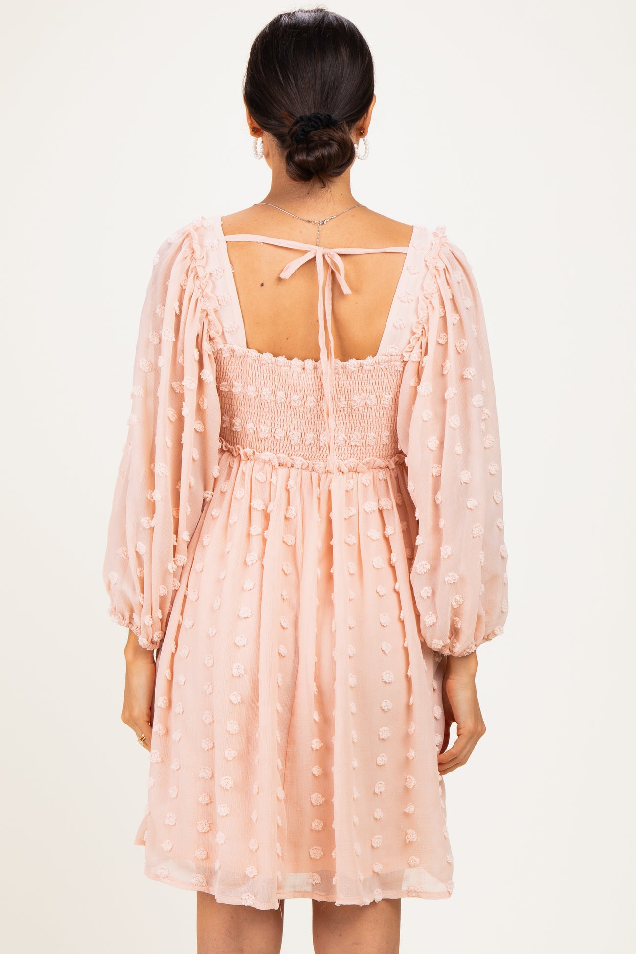 woman wearing a blush pink smocked dress with puff sleeves and dot details, showing the back view