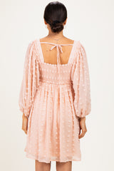 woman wearing a blush pink smocked dress with puff sleeves and dot details, showing the back view