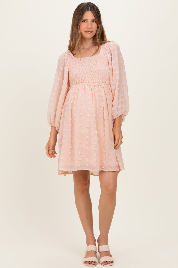 woman wearing a light pink maternity dress with puff sleeves and a smocked bodice, standing in a relaxed pose