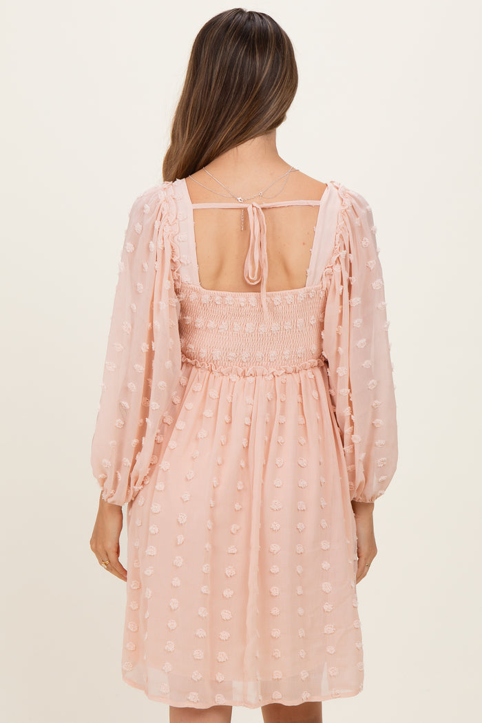 woman wearing a blush pink maternity dress with smocked bodice and puff sleeves, seen from the back