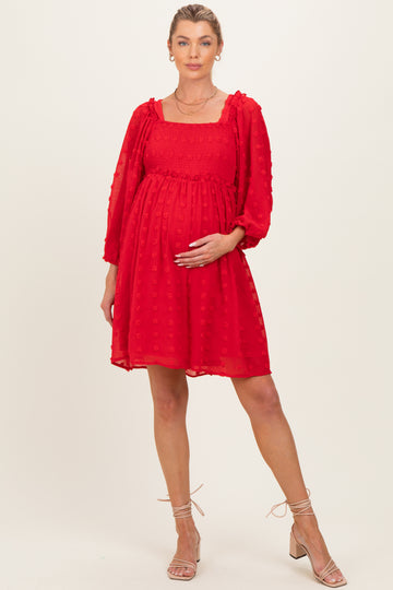 woman wearing a red maternity dress with puff sleeves and a smocked bodice, gently cradling her baby bump