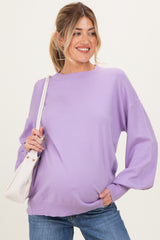 woman wearing a lavender maternity sweater with balloon sleeves and a visible baby bump, holding a white handbag