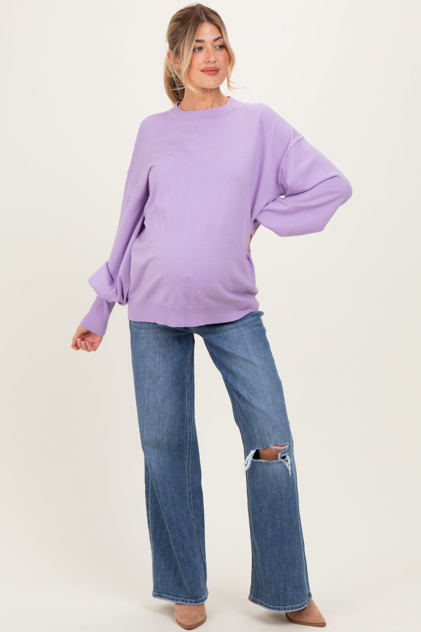 woman wearing a lavender oversized maternity sweater and distressed blue jeans, showcasing her baby bump