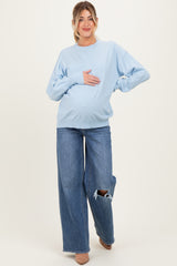 woman wearing a light blue oversized maternity sweater and distressed wide-leg jeans, holding her baby bump