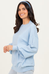 woman wearing a light blue oversized sweater with balloon sleeves and a headband, smiling to the side