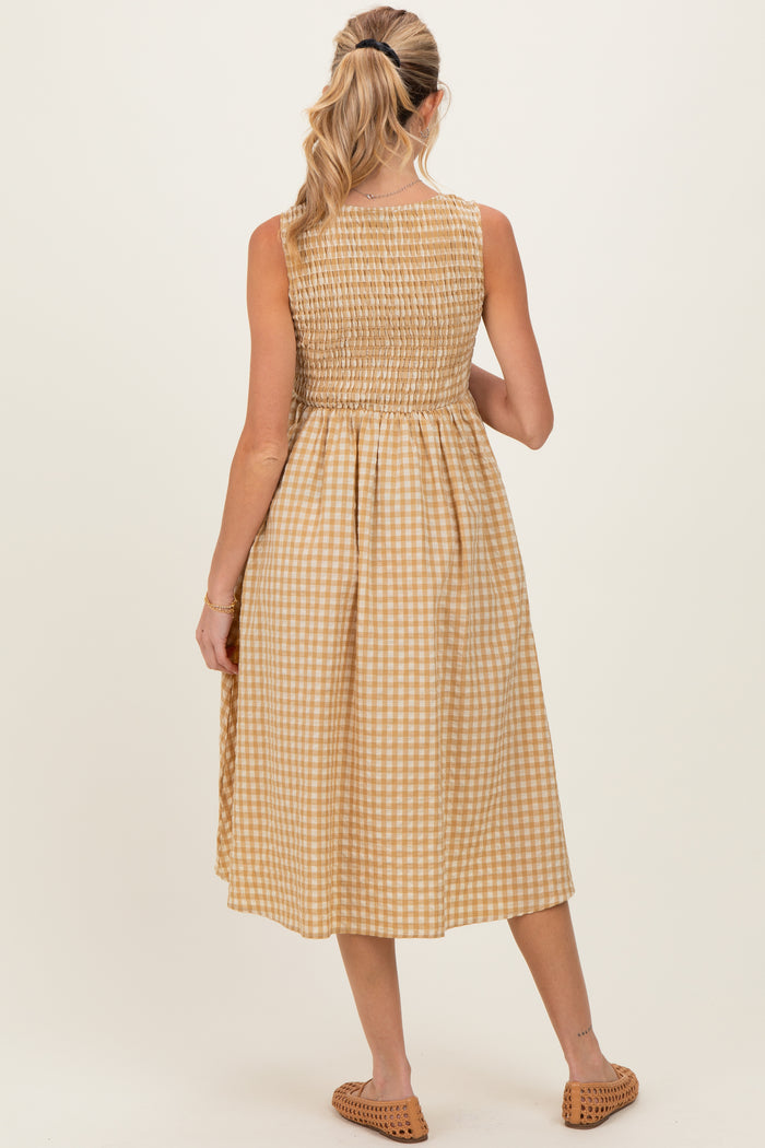 woman wearing a gingham pattern midi maternity dress with a smocked bodice and back pleating, showing her baby bump