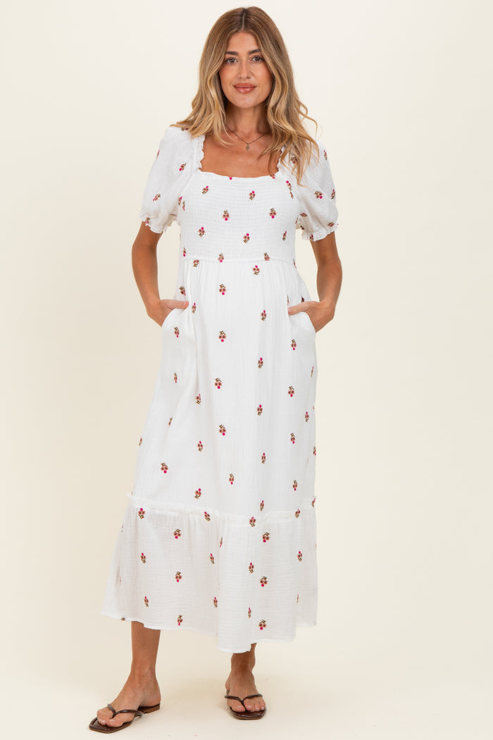 woman wearing a white floral maternity maxi dress with puff sleeves and pockets, showcasing her baby bump