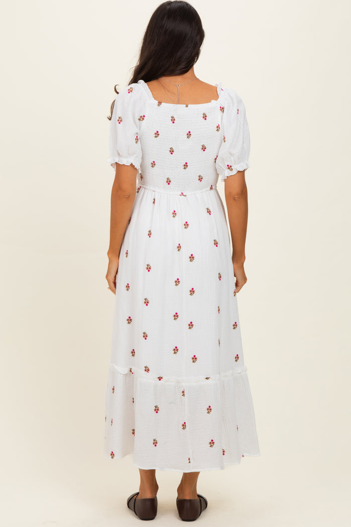 woman wearing a white floral maxi dress with puff sleeves and a tiered skirt, standing with her back to the camera