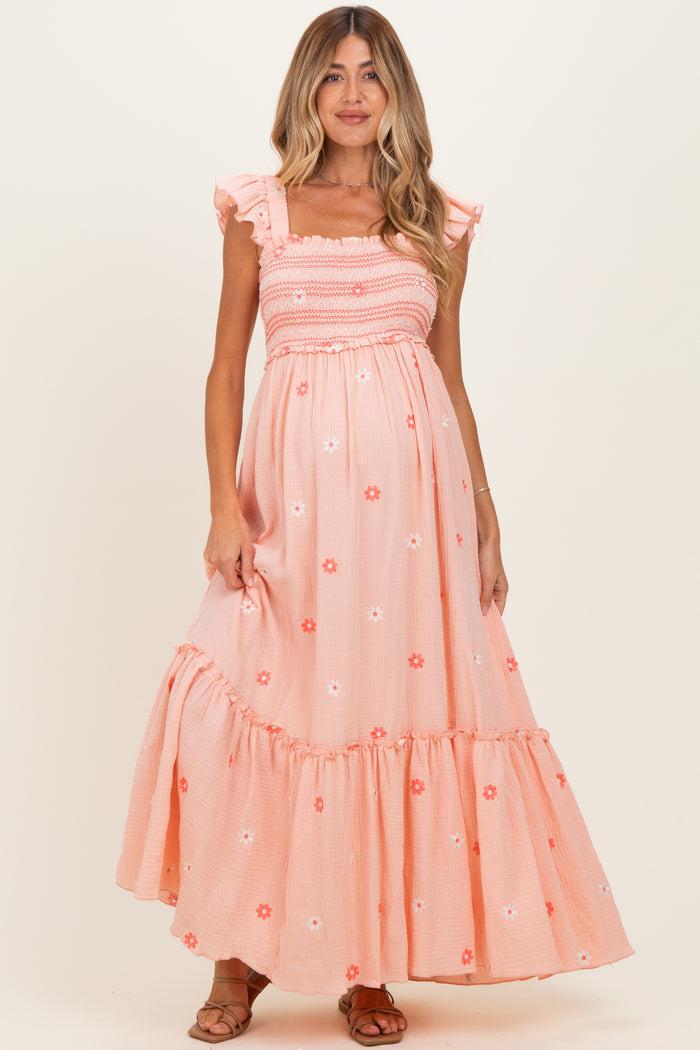 woman wearing a coral floral print maternity maxi dress with ruffled sleeves and a smocked bodice, showcasing her baby bump
