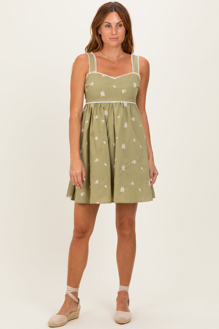 woman wearing a green floral embroidered sundress with spaghetti straps and scalloped trim