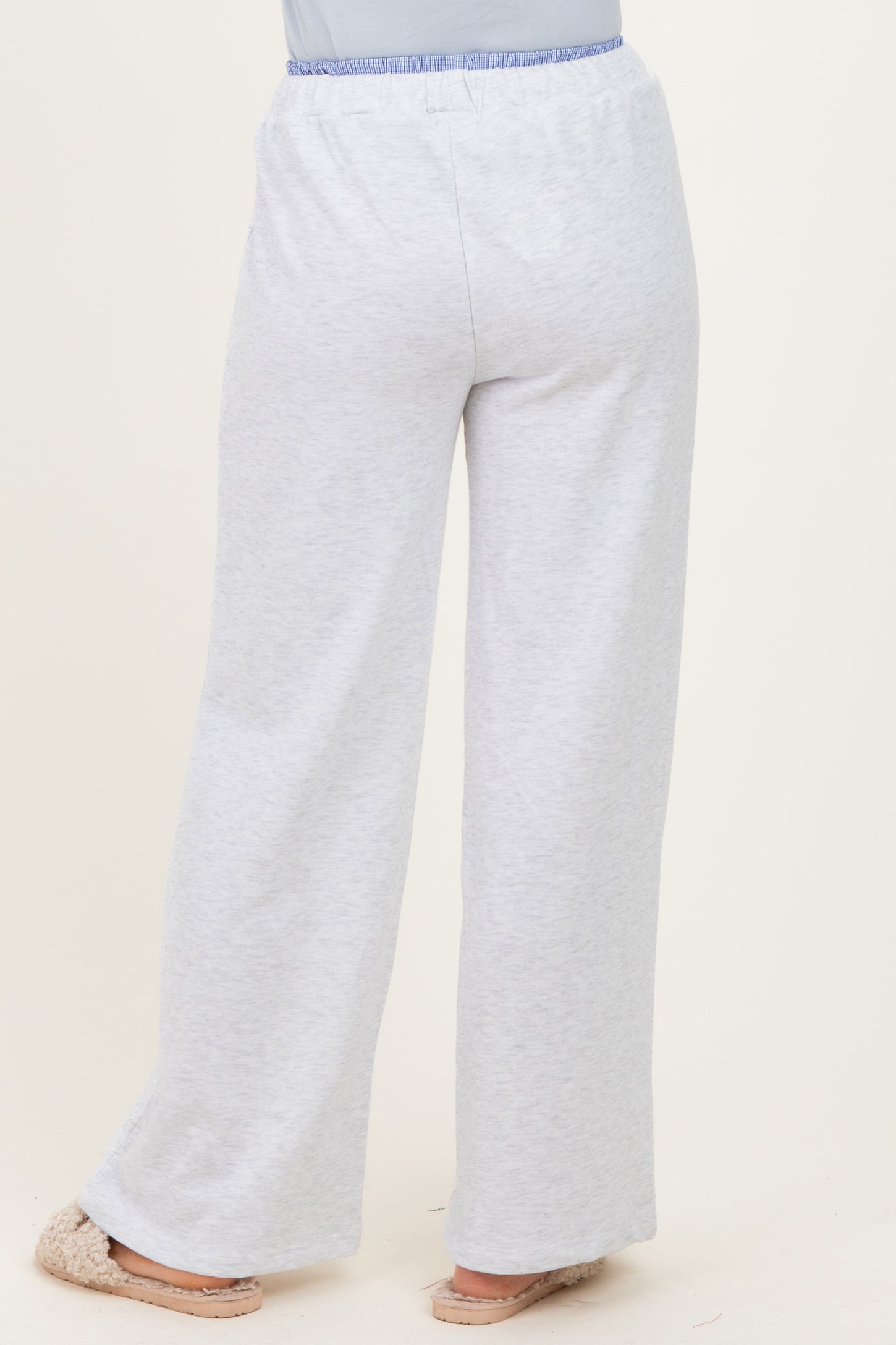 woman wearing light grey wide-leg lounge pants with an elastic waistband and light blue accent, standing with back to camera