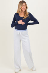 woman wearing a navy long sleeve maternity top and light gray wide-leg maternity pants, holding her baby bump