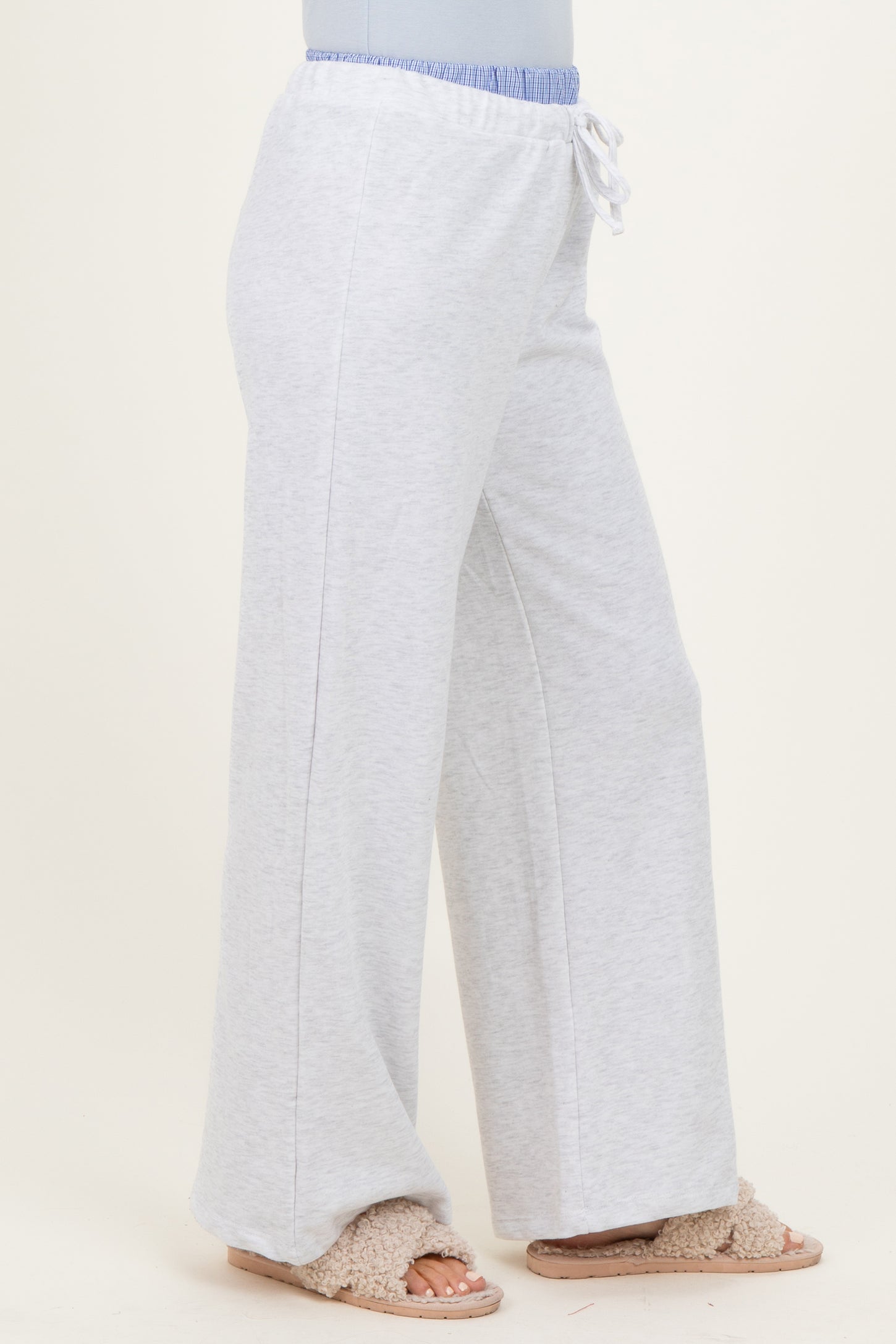 woman wearing light gray wide-leg sweatpants with an elastic waistband and drawstring detail, paired with cozy slippers