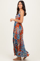 woman wearing an orange floral maxi dress with blue and green patterns and spaghetti straps, standing sideways