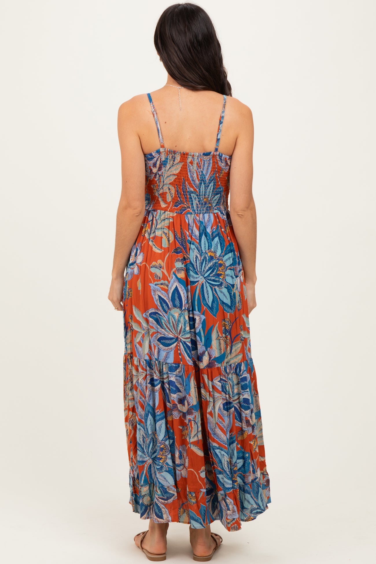 woman wearing a back view of a colorful floral maxi dress with spaghetti straps and a tiered skirt