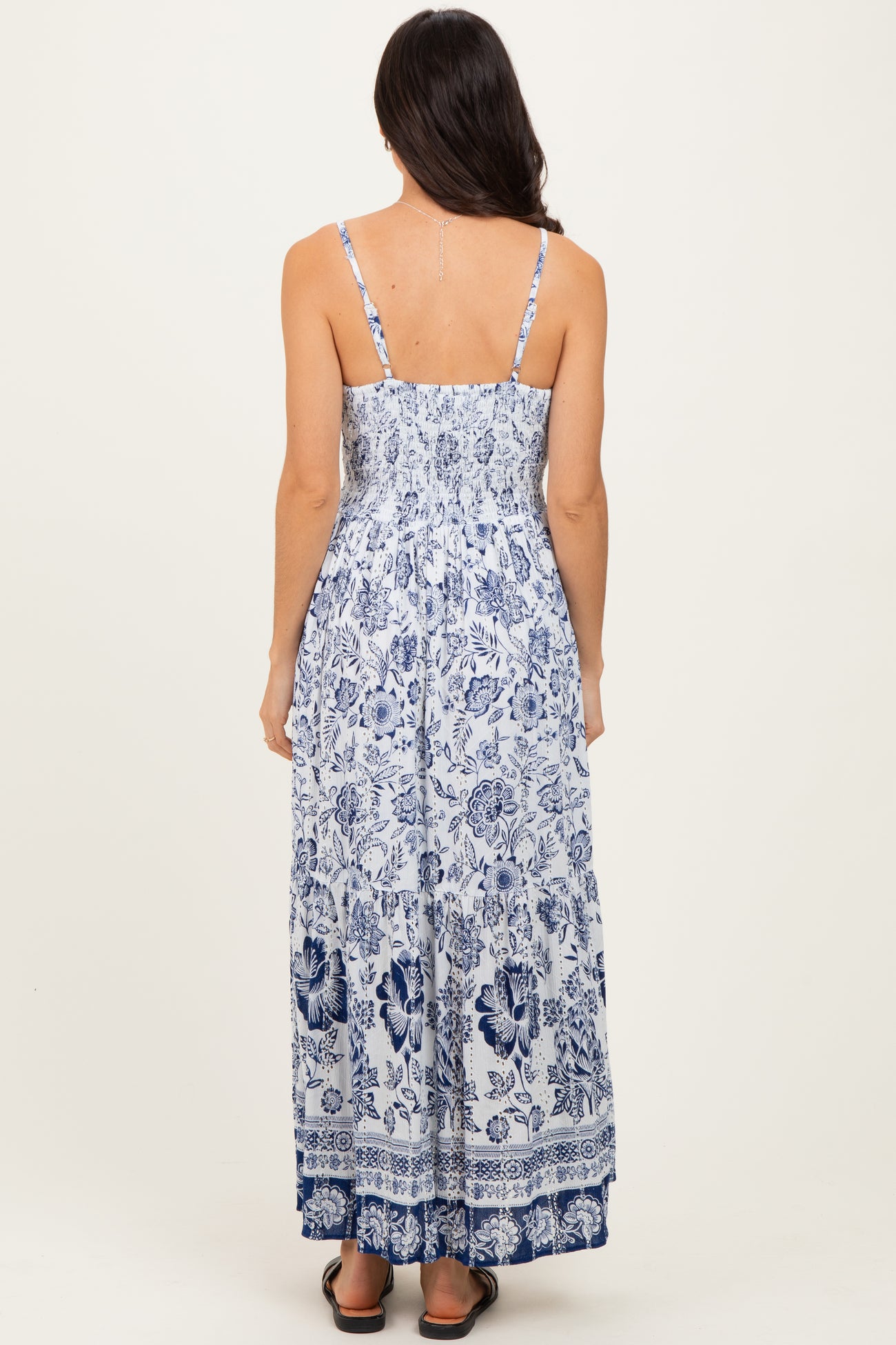 woman wearing a white and blue floral maxi dress with adjustable straps and a smocked back