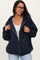 woman wearing a dark navy maternity zip-up hoodie with a front pocket and relaxed fit, smiling and adjusting the hood