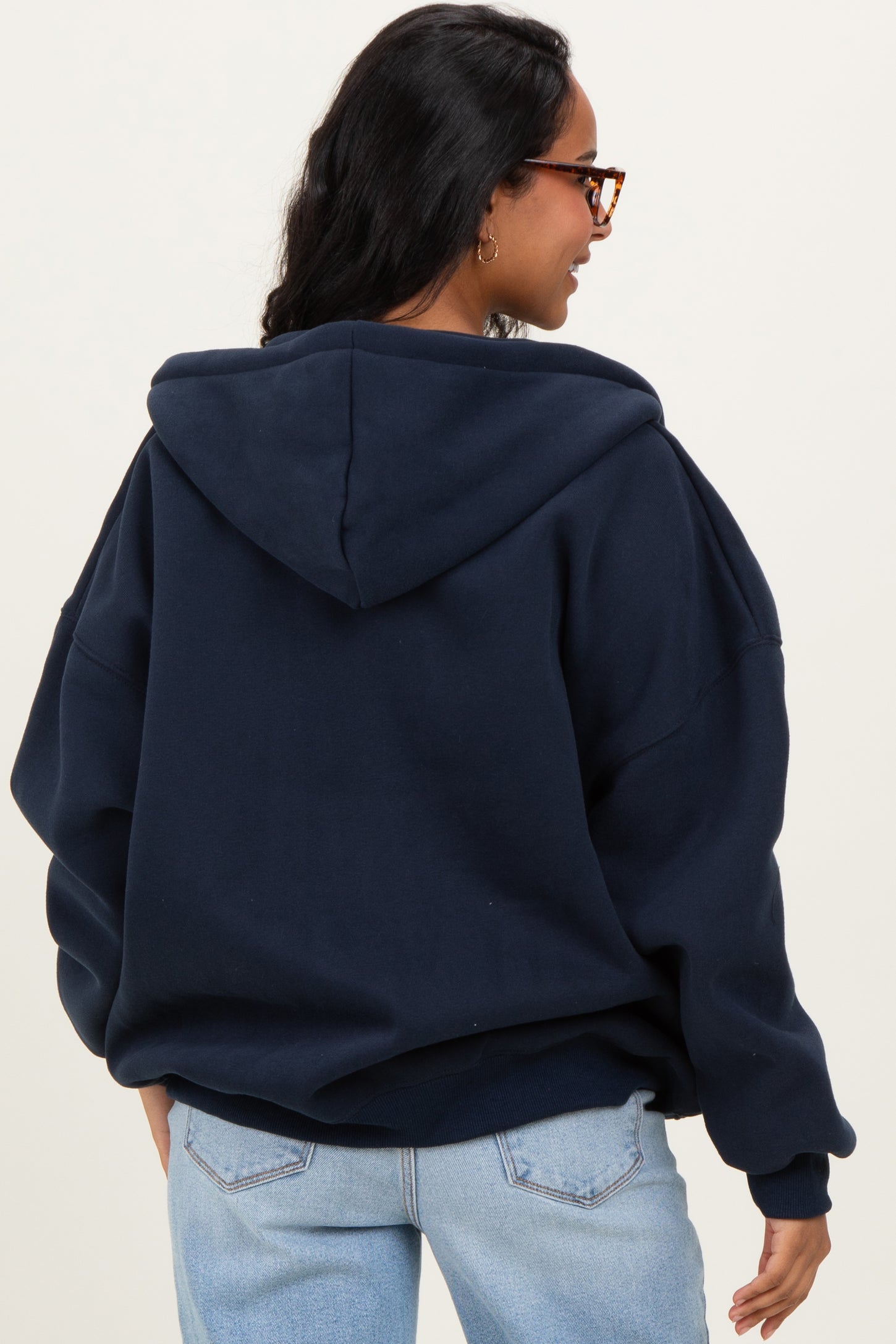 woman wearing a navy blue oversized maternity hoodie with a hood and a relaxed fit, seen from the back