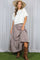 woman wearing a white cropped cardigan and a brown stripe tiered maxi skirt, paired with brown knee-high boots and a wide-brim hat