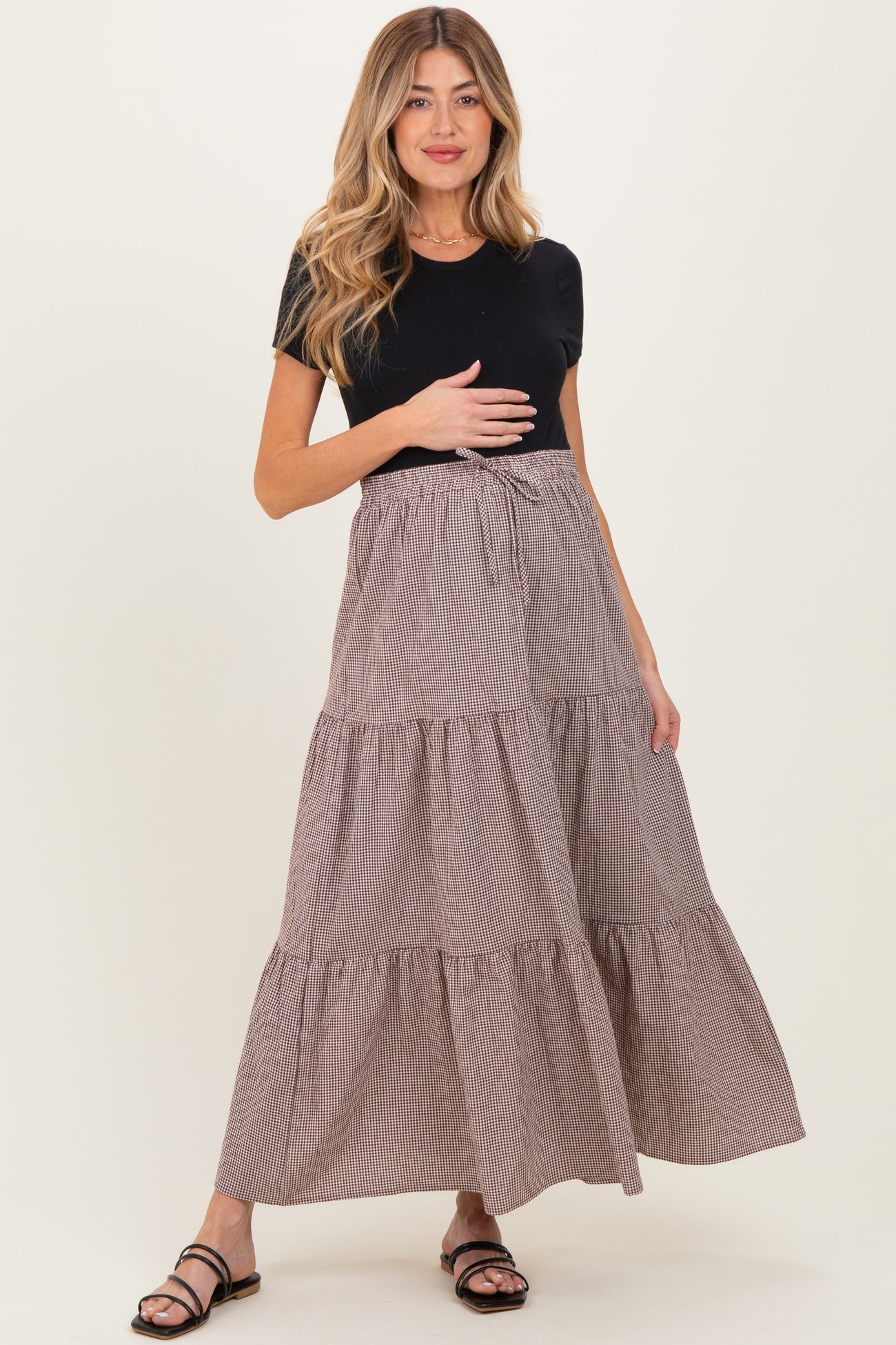woman wearing a black short sleeve top and a brown striped maternity maxi skirt, holding her baby bump