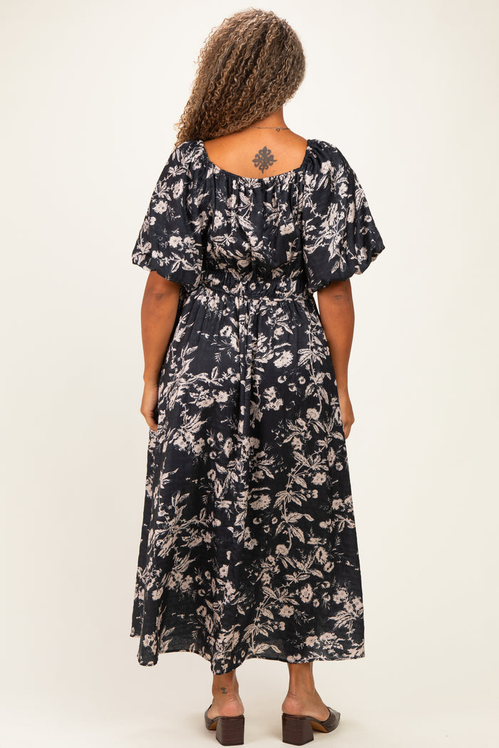 woman wearing a flowy black floral plus-size maxi dress with short puff sleeves and a cinched waist, viewed from the back