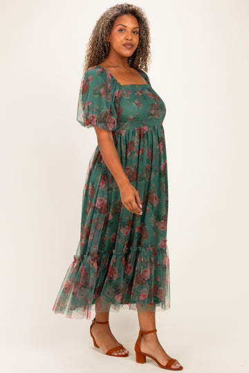 woman wearing a green floral plus-size maxi dress with puff sleeves and a tiered hem, standing on a light background
