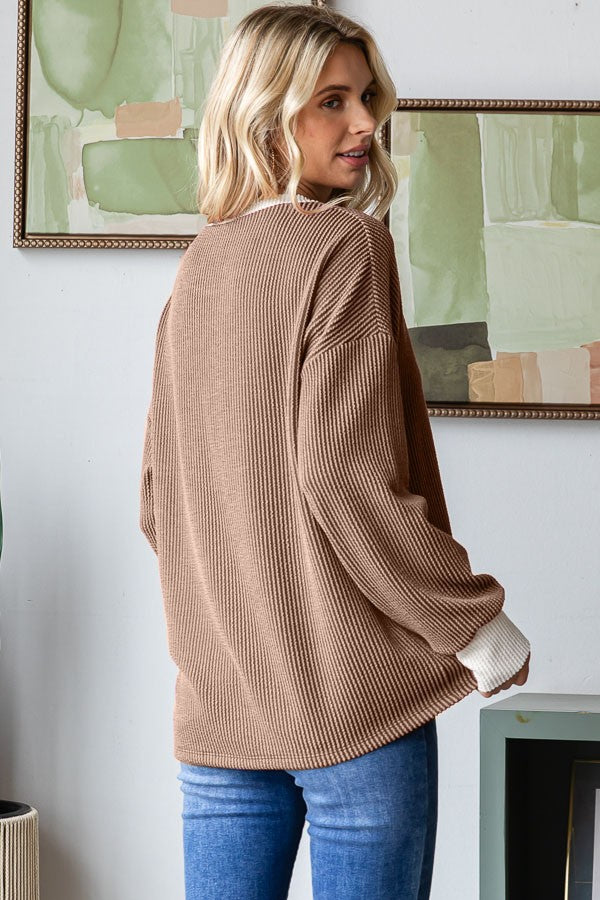 woman wearing a brown ribbed oversized sweater with white cuffs and blue jeans, viewed from the back