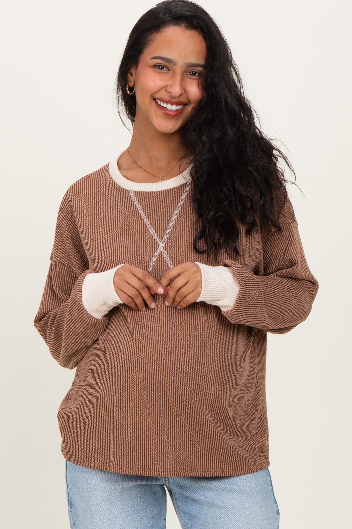 woman wearing a brown maternity sweater with cream accents and showing her baby bump